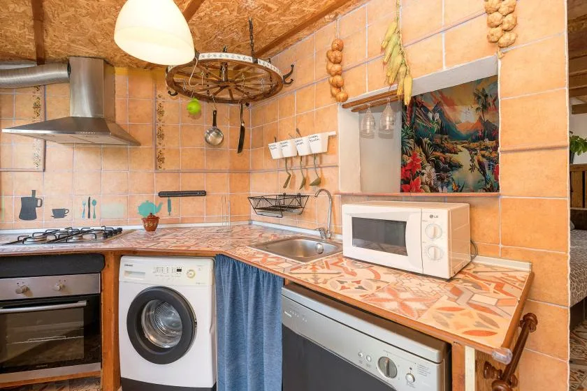 A compact kitchen with tiled counters, a washing machine, and a microwave.