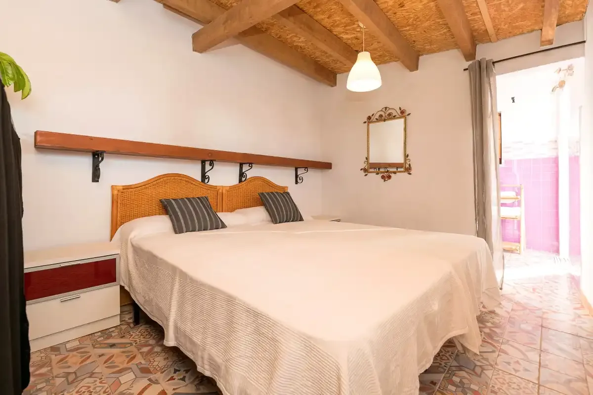 A bedroom with a large bed beneath exposed wooden ceiling beams.