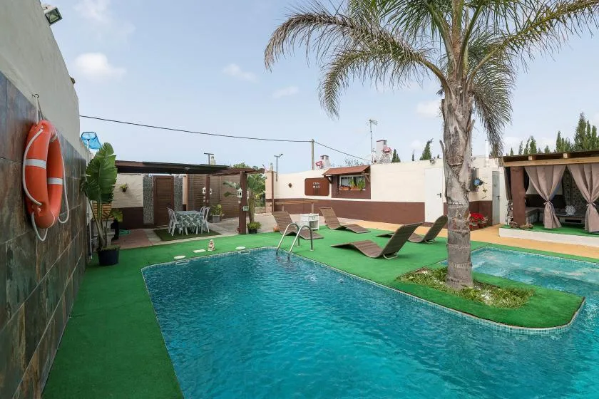 An outdoor swimming pool is surrounded by green turf and lounge seating.
