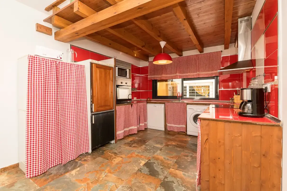 A compact kitchen with red tile, wood cabinetry, and a wood-beamed ceiling.
