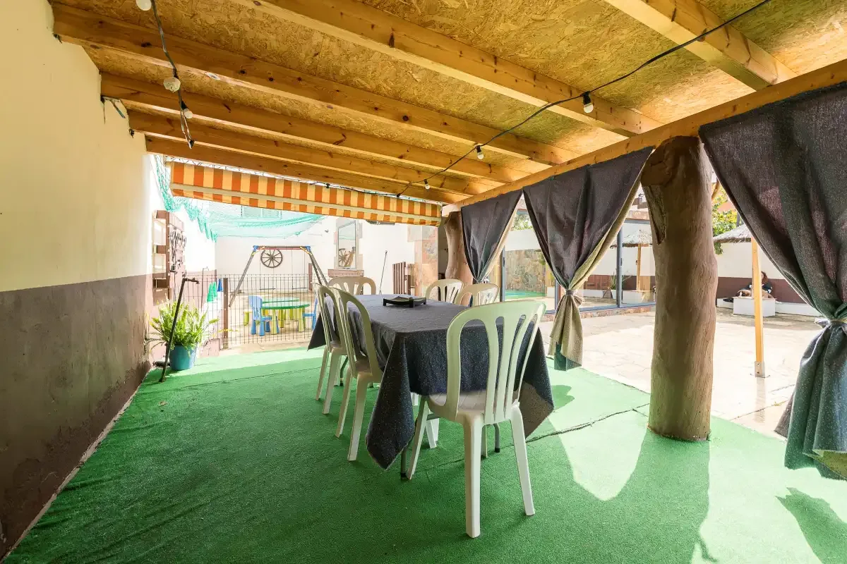 A covered outdoor dining area with a table and chairs on green flooring.