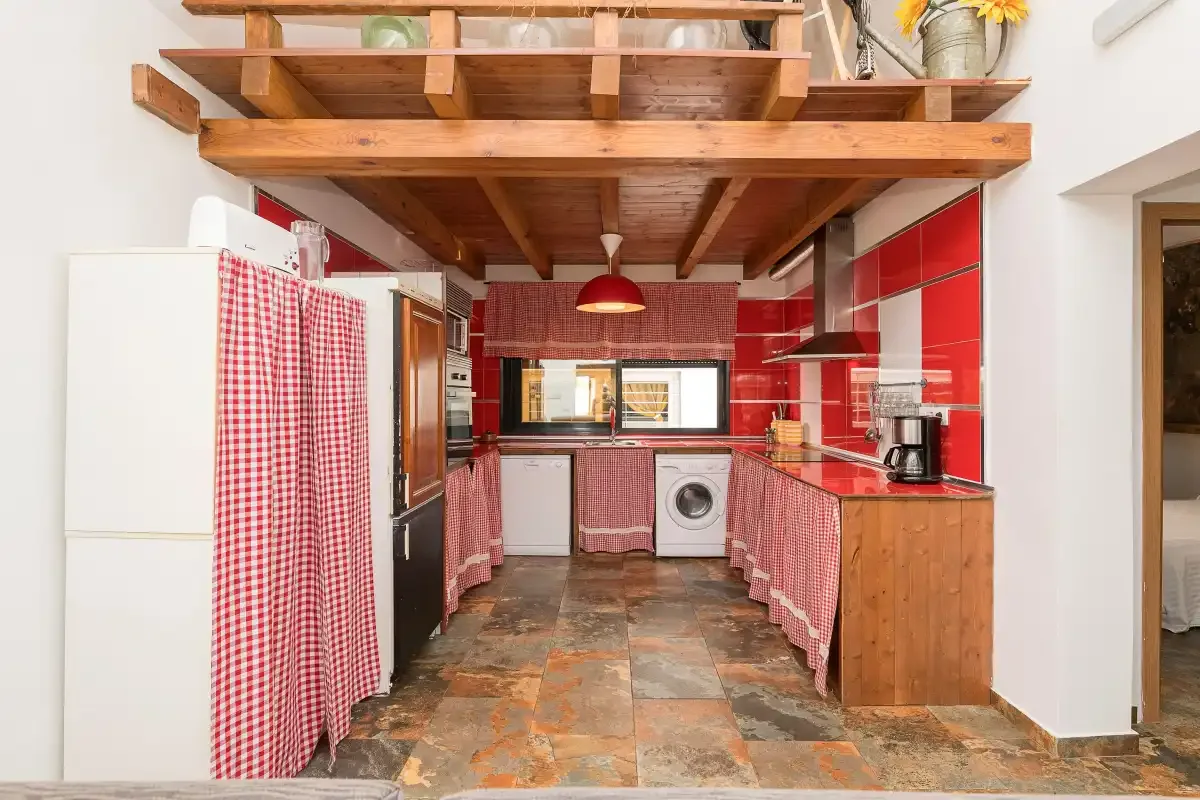 A kitchen with red-and-white checked curtains and exposed wooden ceiling beams.