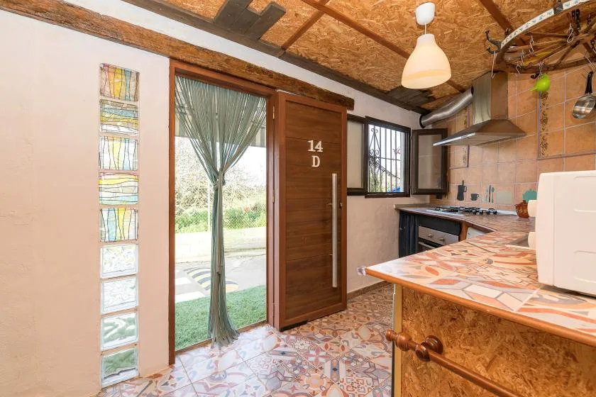A rustic kitchen with a tiled counter and a glass door opening to the outdoors.