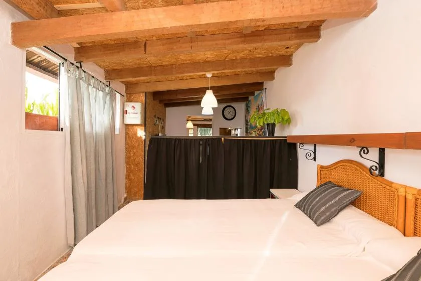 A bedroom with a white bed beneath exposed wooden ceiling beams.