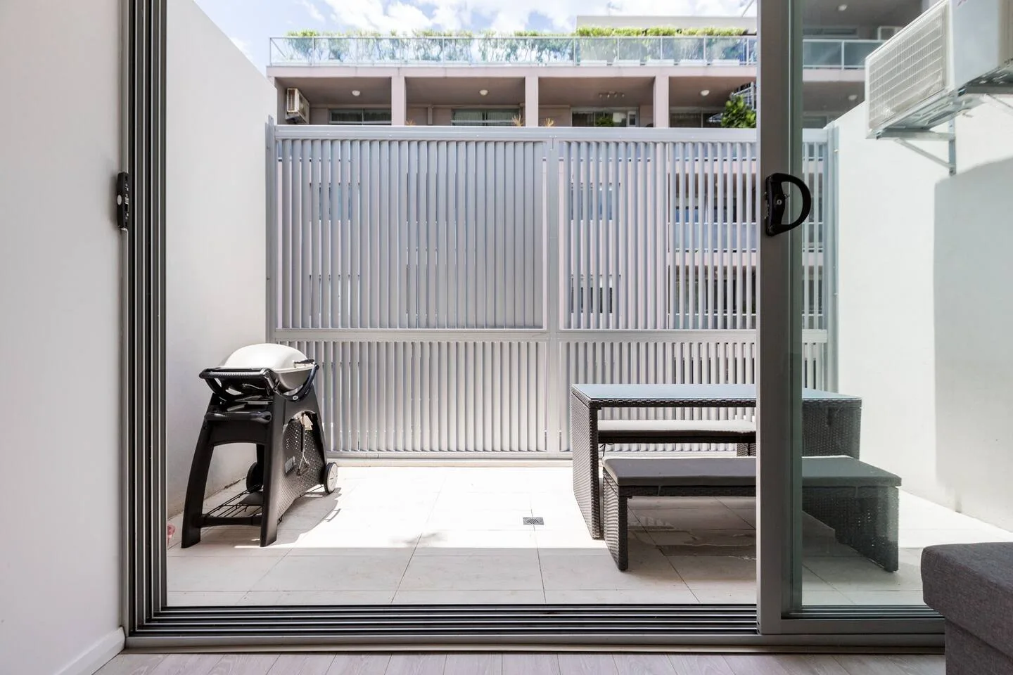 A small outdoor patio with a grill and seating beside a sliding glass door.