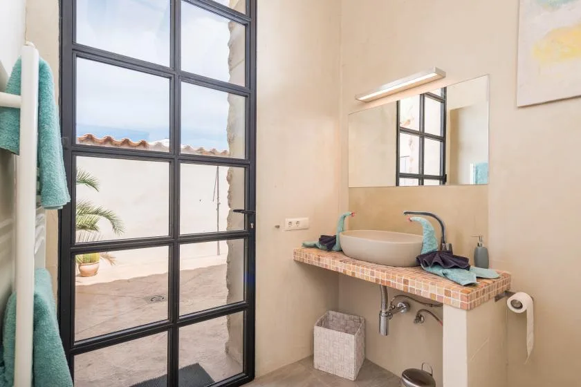 Un lavabo de baño con espejo está junto a una gran puerta de vidrio con marco negro.