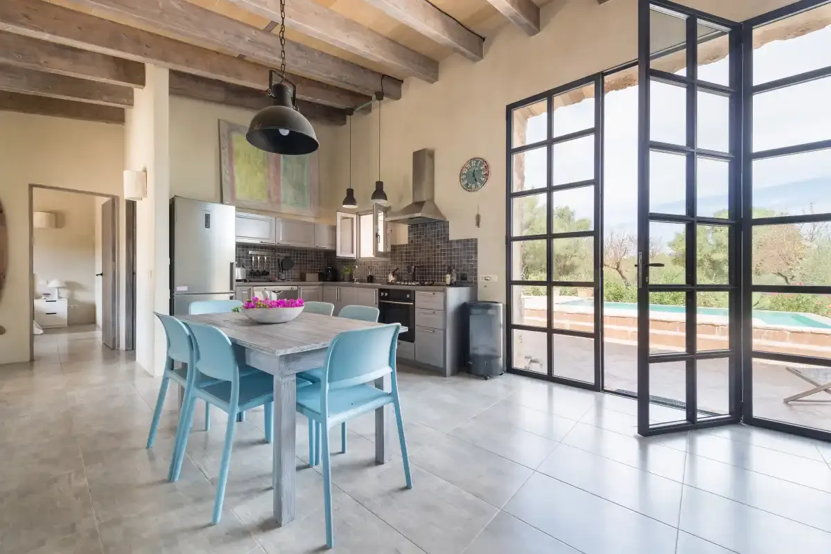 Comedor con mesa y asientos junto a una cocina y grandes puertas de cristal.