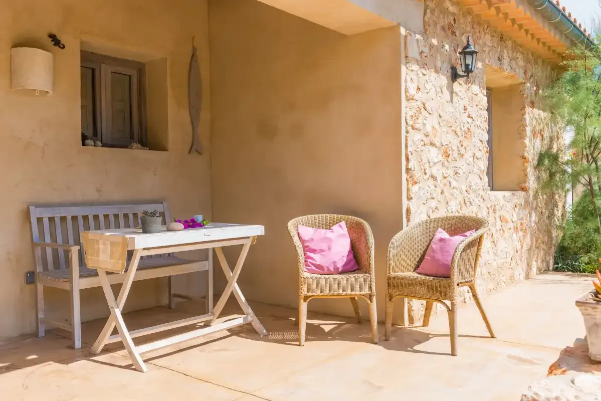 Un patio sombreado con una mesa y asientos con cojines junto a un muro de piedra.
