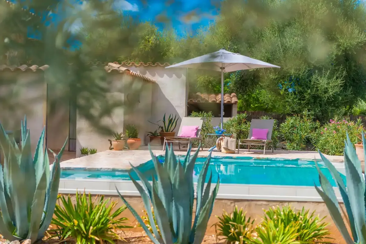 Una piscina está junto a un patio con asientos y una sombrilla.
