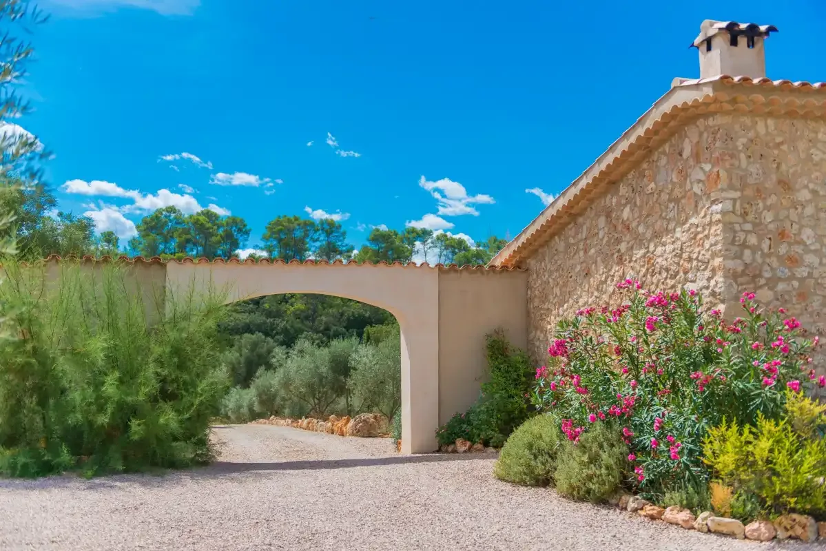Un camino de grava atraviesa un arco de jardín junto a un edificio de piedra.