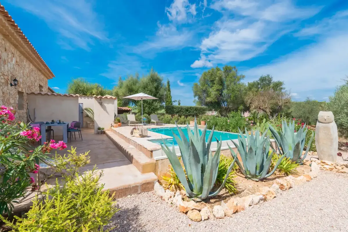Una piscina al aire libre está junto a un patio y un jardín ajardinado.
