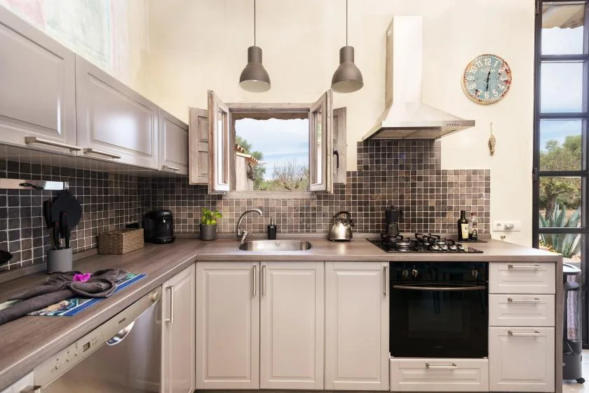 Una cocina luminosa con gabinetes claros, azulejos oscuros y una ventana sobre el fregadero.