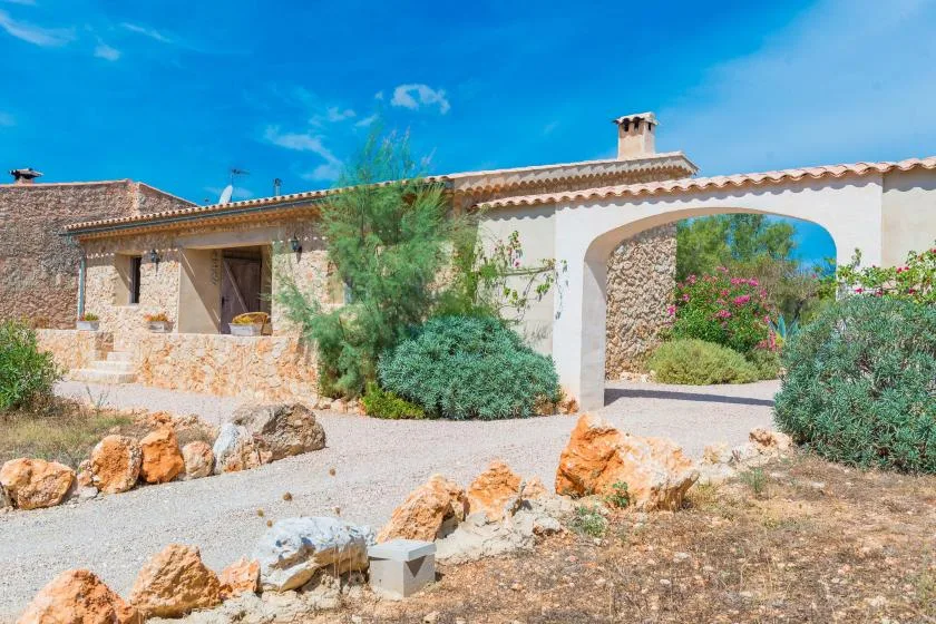 Una construcción de piedra junto a una entrada arqueada al jardín y un camino de grava.