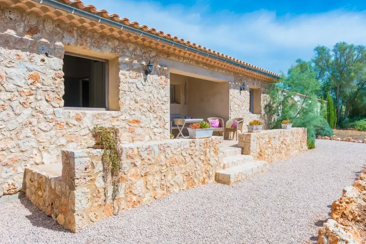 El exterior de una casa de piedra da a un patio de grava con asientos al aire libre.