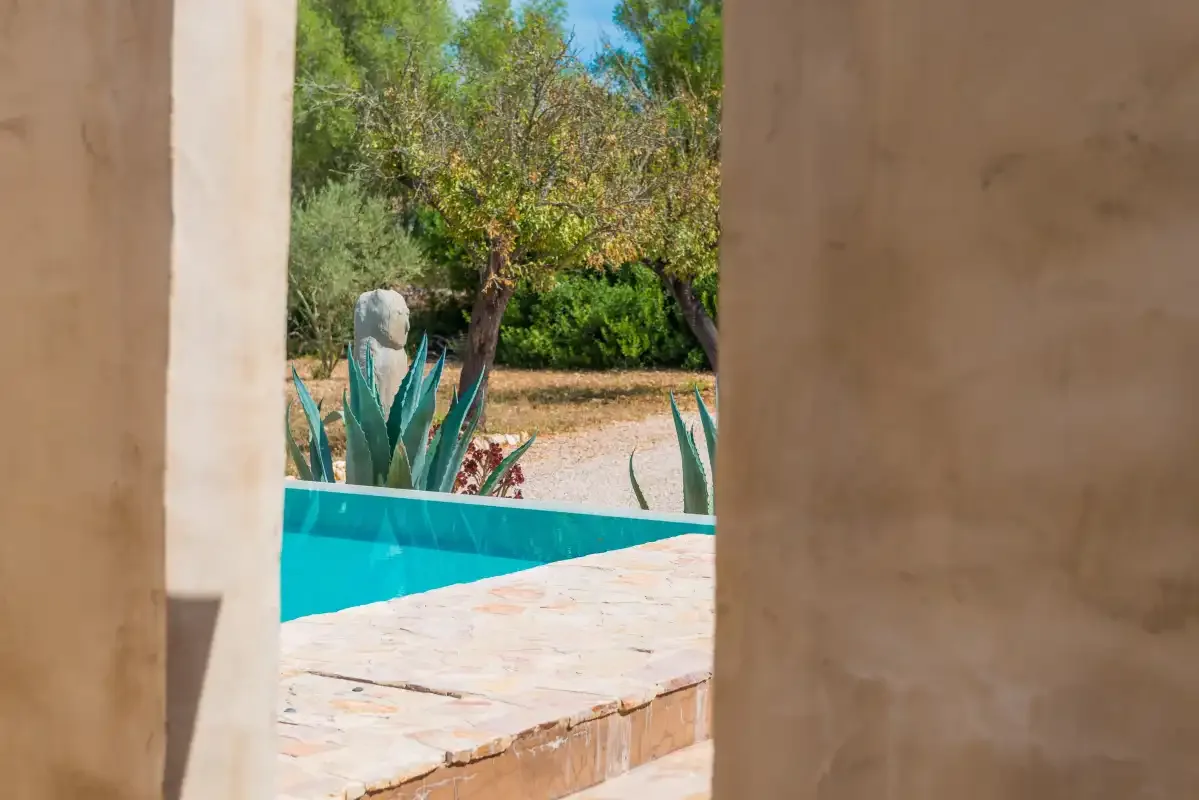 Una piscina turquesa y el jardín circundante se ven a través de una puerta.