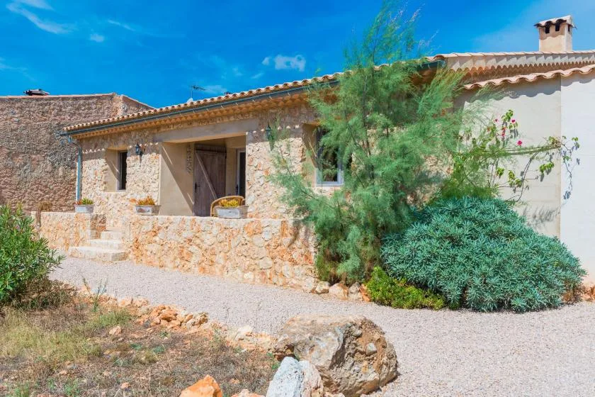 Una casa de piedra con entrada cubierta, arbustos y un camino de grava.