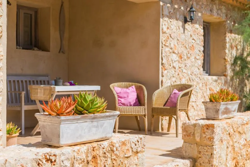 Un patio soleado de piedra tiene asientos de mimbre y macetas con suculentas.