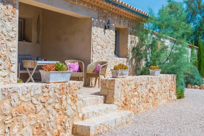 Un patio de piedra con asientos, plantas en macetas y escalones hacia un camino de grava.