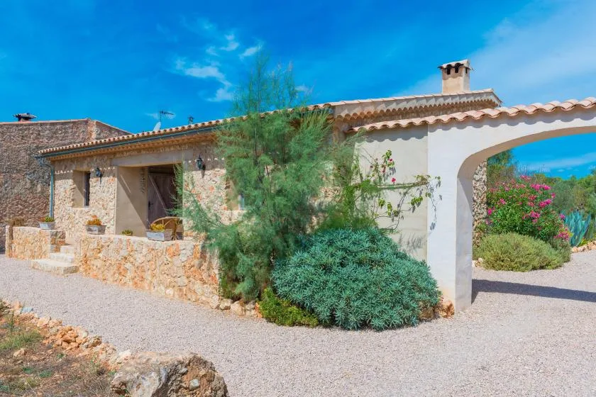 Una casa de piedra con techo de tejas está junto a un patio de grava y un jardín.