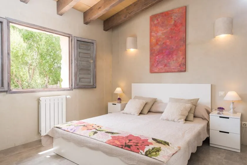Un dormitorio con una cama doble, mesillas de noche y una ventana con vistas a la vegetación.