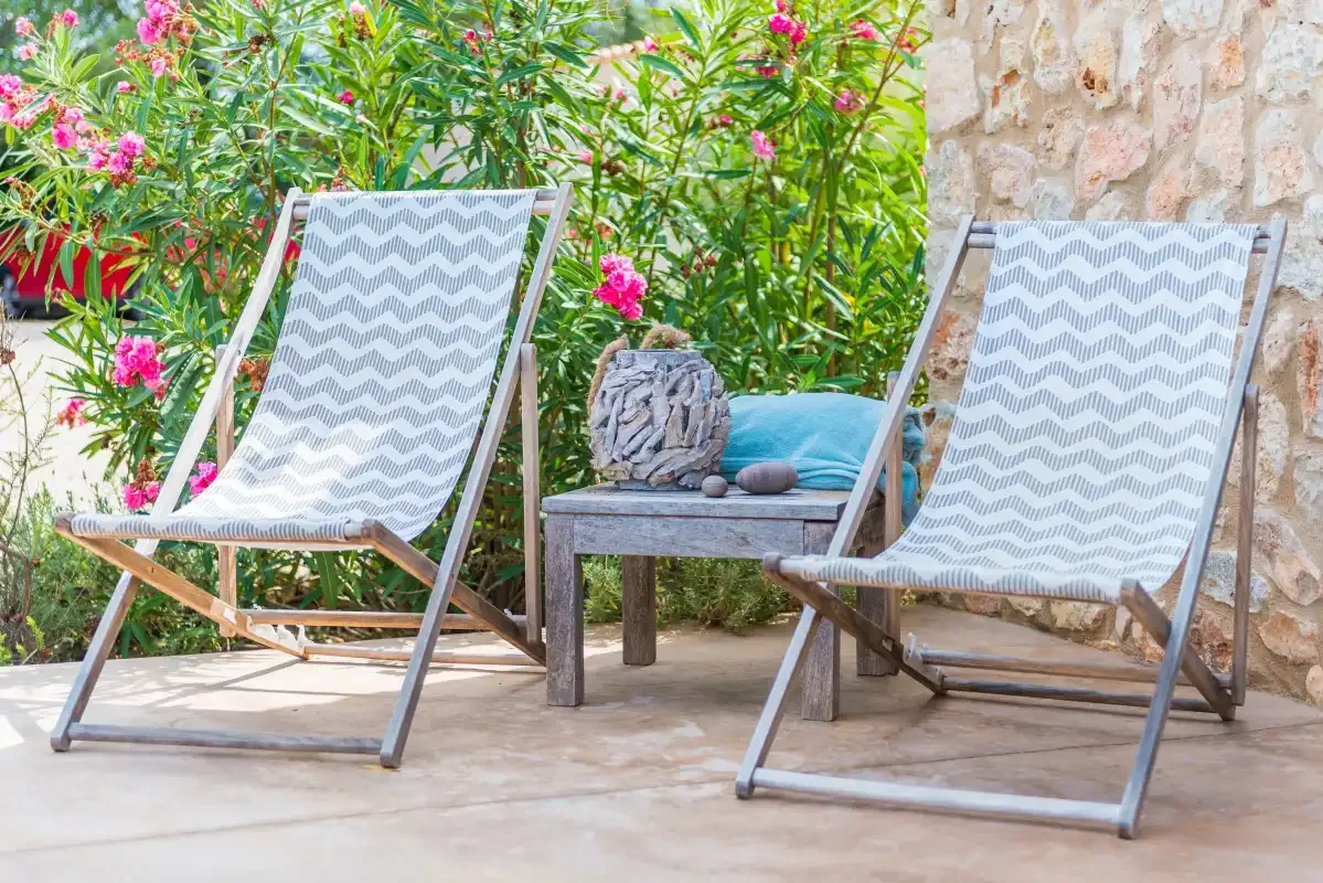 Zona de estar al aire libre con dos sillas reclinables junto a plantas con flores.