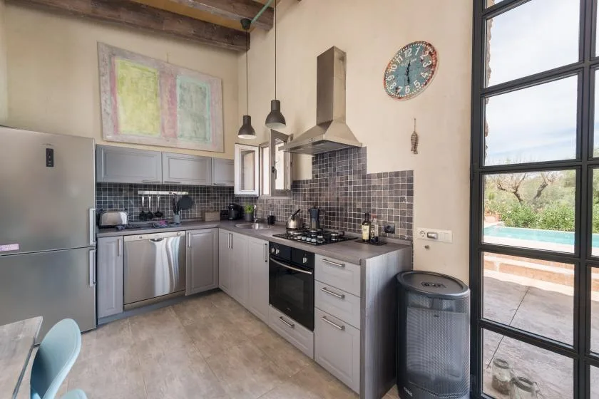 Una cocina moderna con gabinetes grises, un salpicadero de azulejos oscuros y una ventana grande.