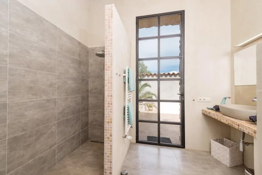 Un baño luminoso con ducha alicatada, una ventana alta y un lavabo.