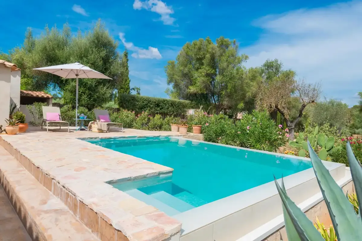 Una piscina exterior está junto a un patio pavimentado con asientos y una sombrilla.