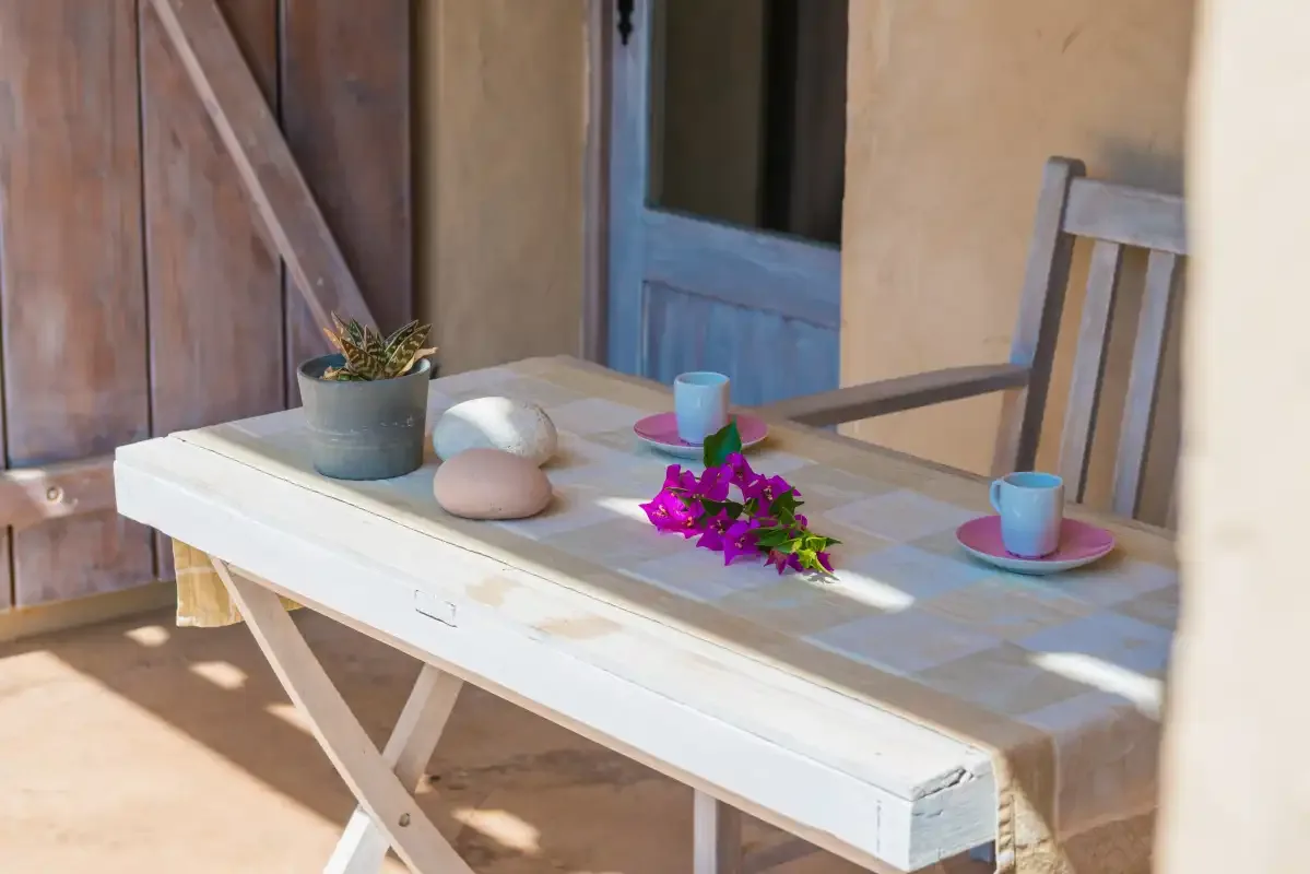 Una mesa de patio con tazas, una planta en maceta y flores.