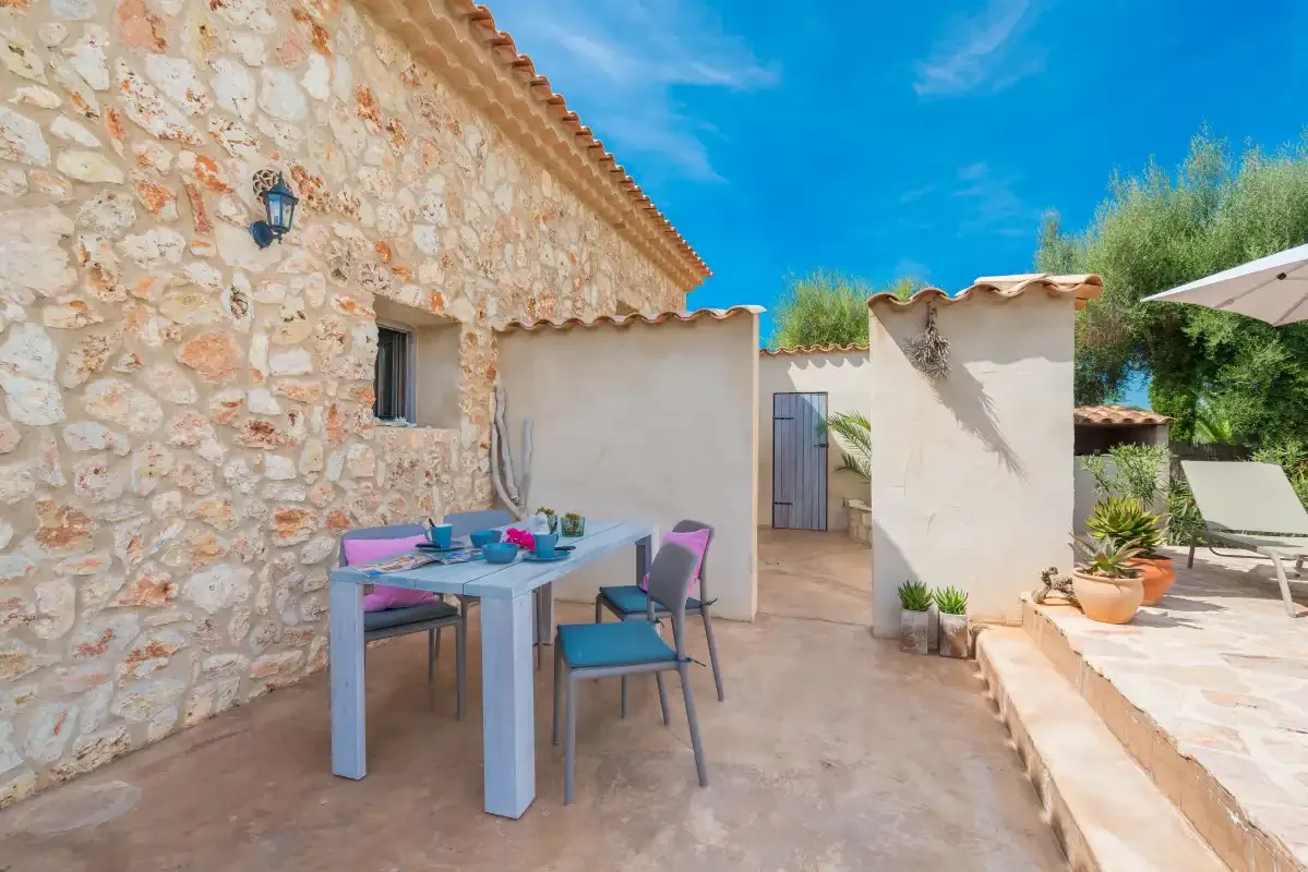 Un patio de piedra tiene una mesa al aire libre y asientos coloridos.