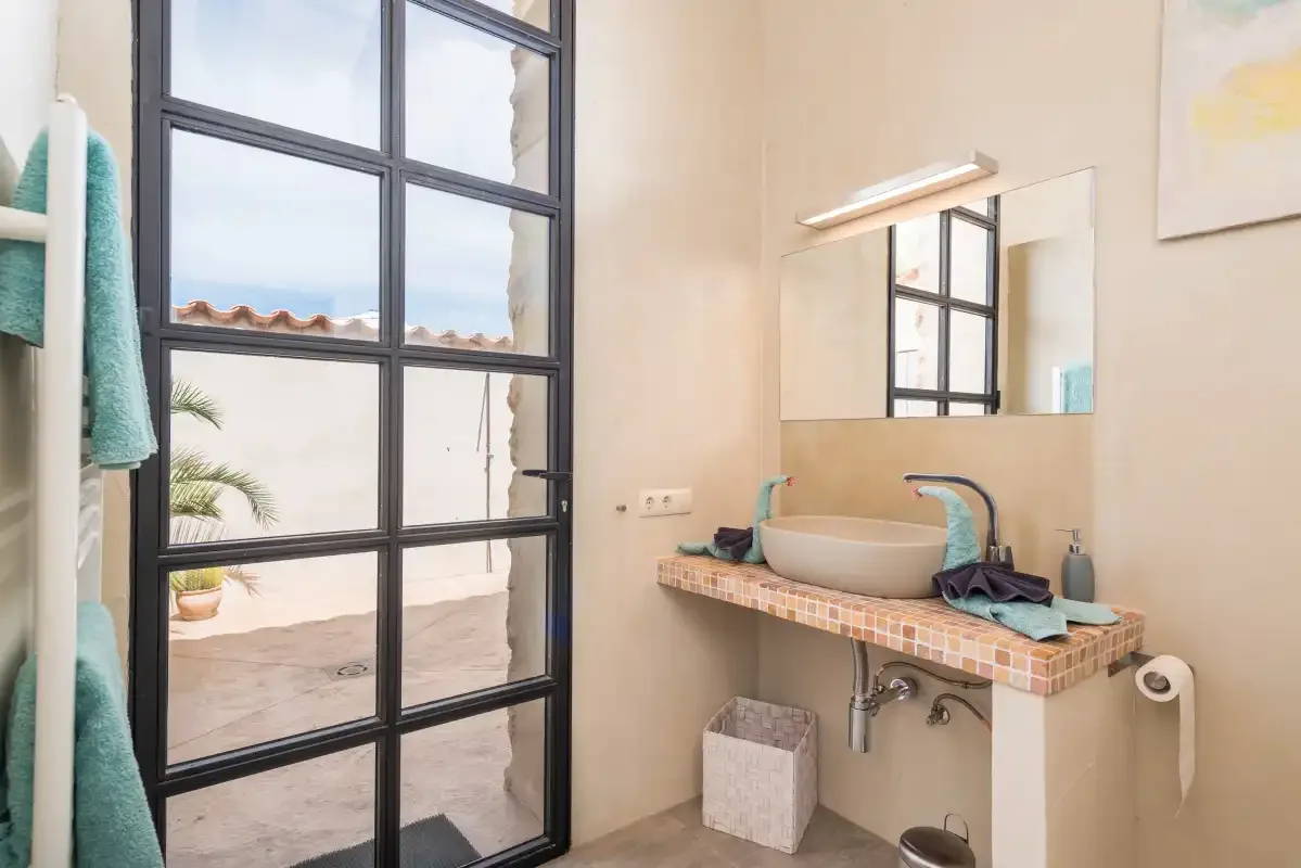 Un baño luminoso con un lavabo sobre encimera y una puerta acristalada con marco negro.
