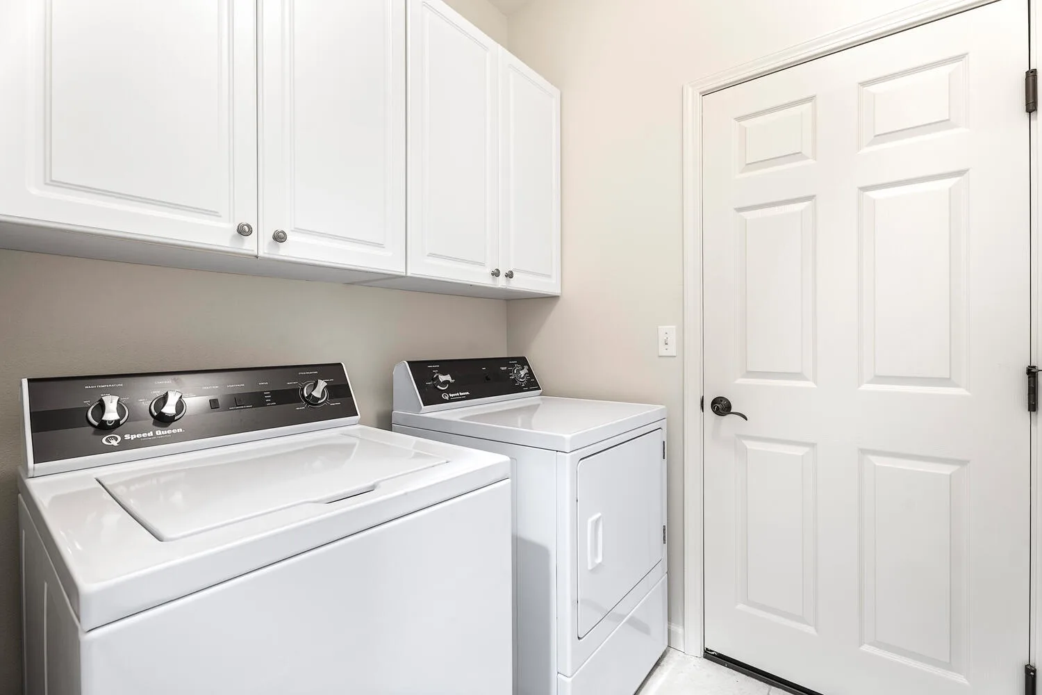 A laundry area with a washer and dryer beneath white cabinets.