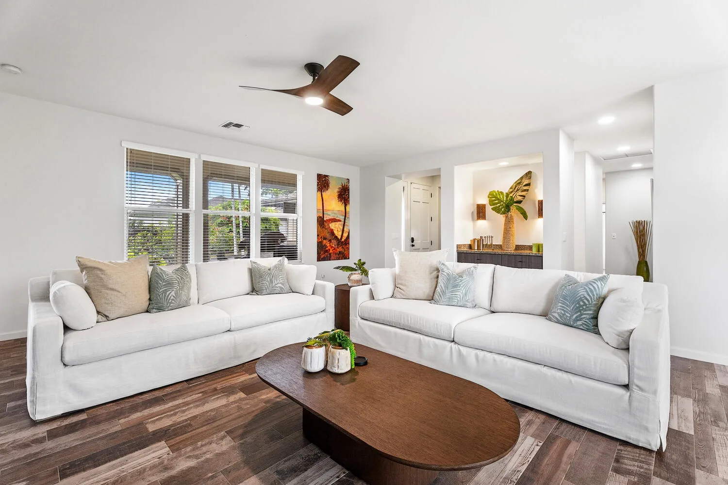 A bright living room with white seating, a wooden coffee table, and large windows.