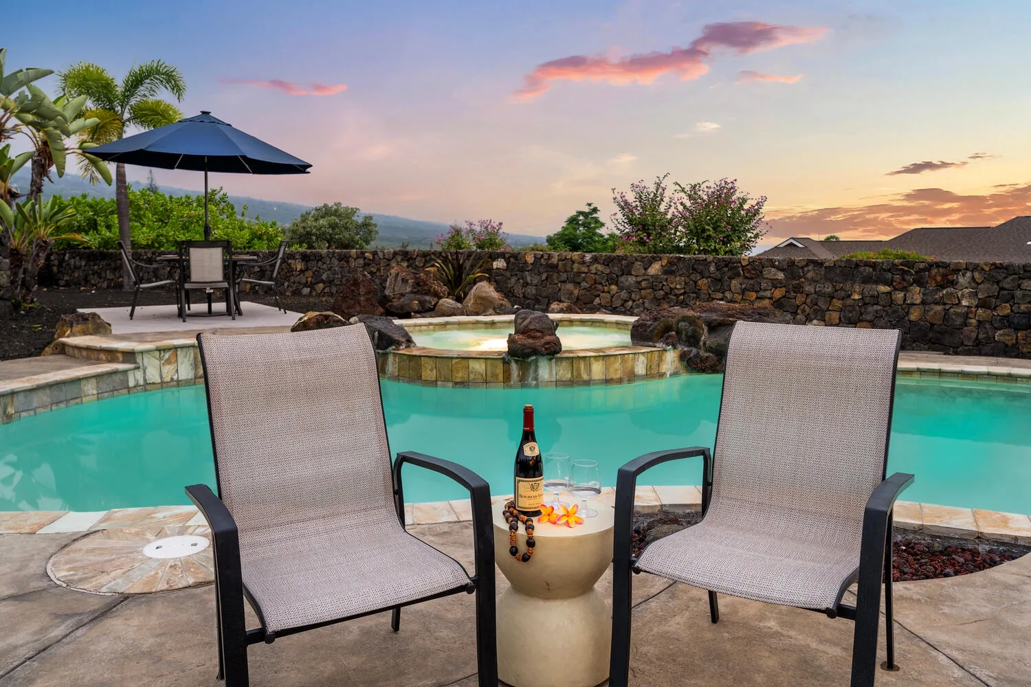 A poolside seating area overlooks a turquoise pool at sunset.