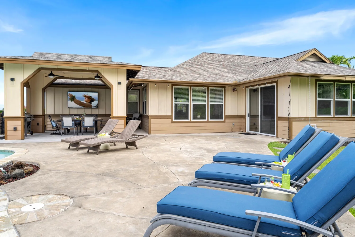A sunny patio with blue lounge seating beside a house and covered outdoor dining area.
