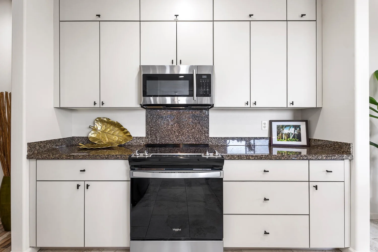 A bright kitchen with white cabinets, a dark countertop, and a stainless steel microwave.