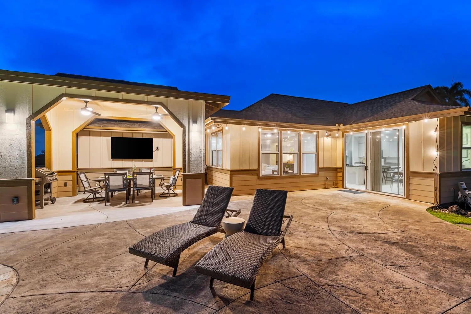 An illuminated outdoor patio with lounge seating, a dining area, and large windows at dusk.