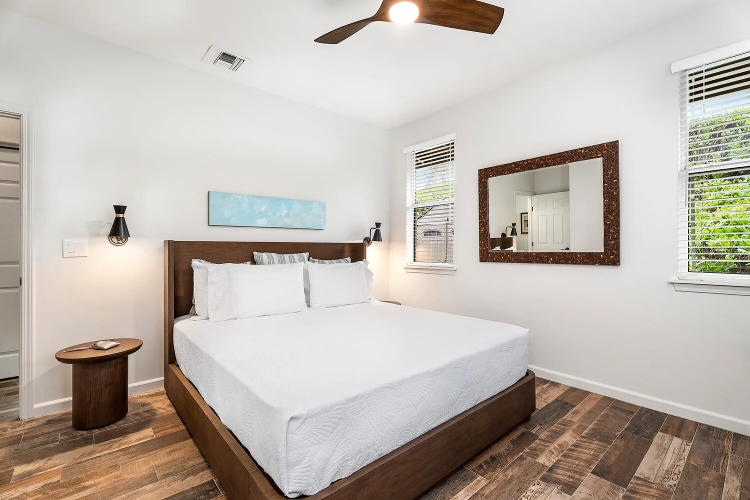 A bright bedroom with a neatly made bed and a large wall mirror.