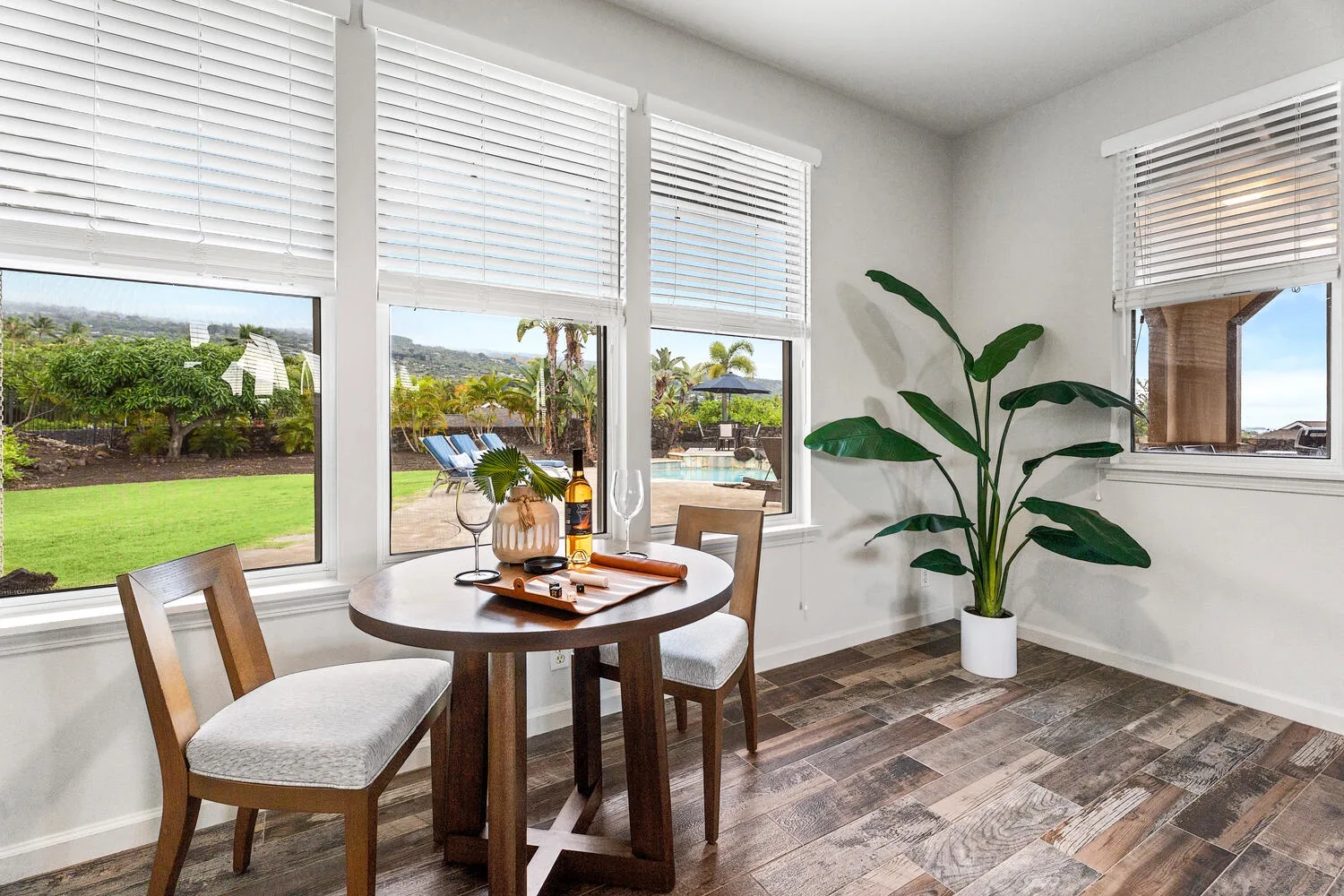 A dining area with a round table and chairs beside windows overlooking greenery.