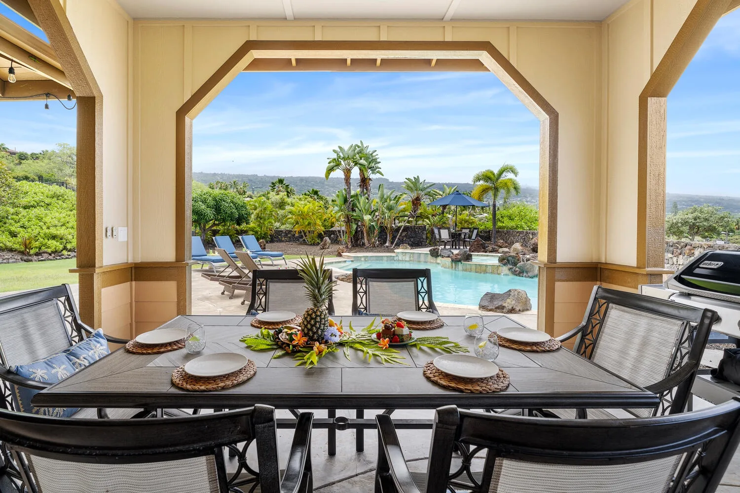 A covered outdoor dining area overlooks a swimming pool and tropical landscaping.