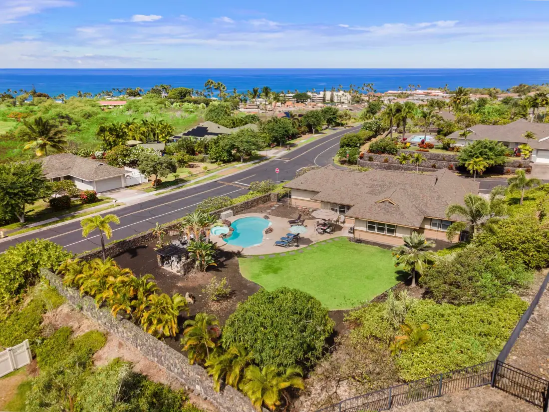Aerial view of a landscaped property with a swimming pool and the ocean in the distance.