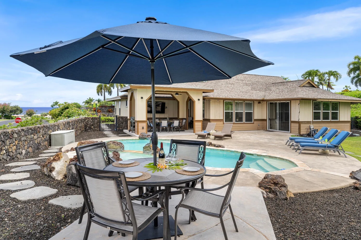 A backyard pool and patio with outdoor seating beneath a large umbrella.