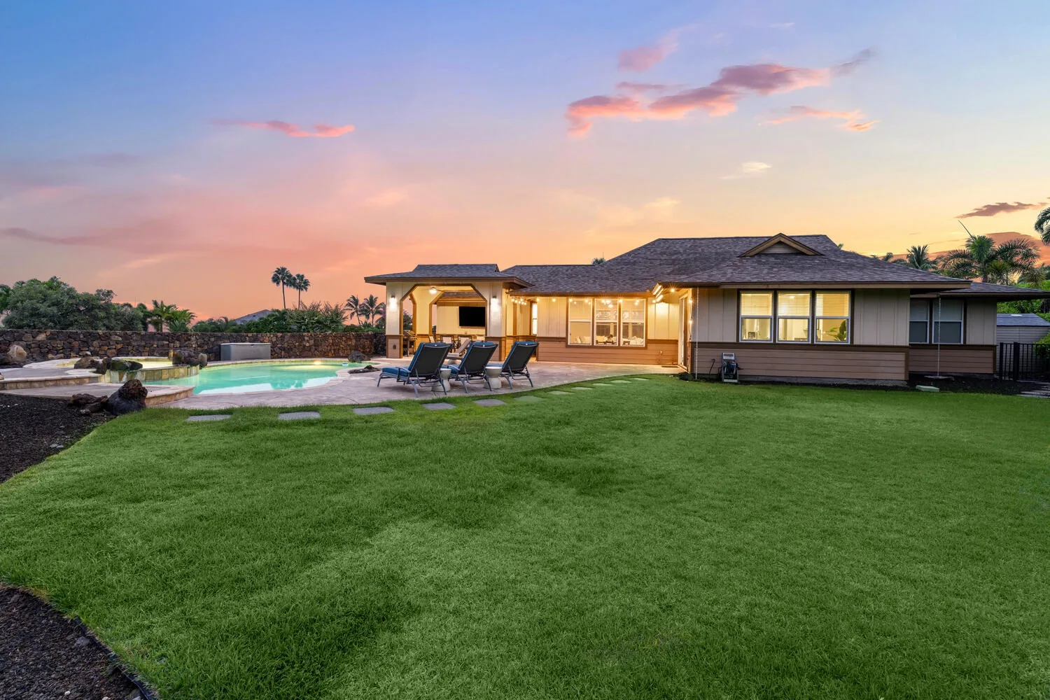 A single-story house overlooks a lawn and swimming pool at sunset.
