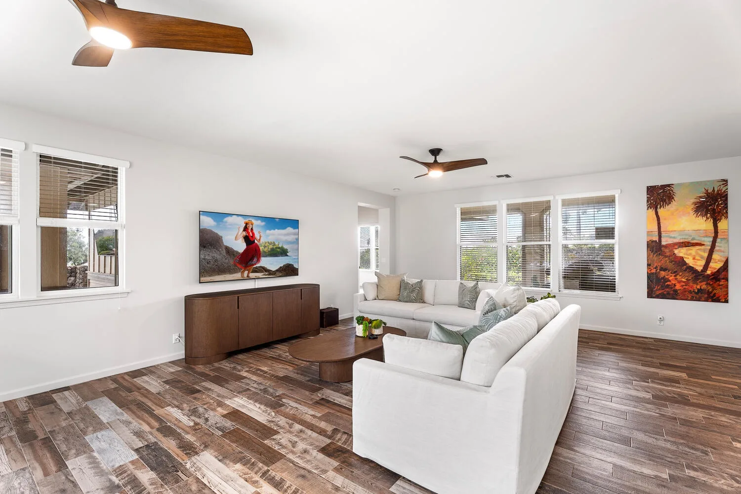 A bright living room with white seating, wide windows, and colorful wall art.