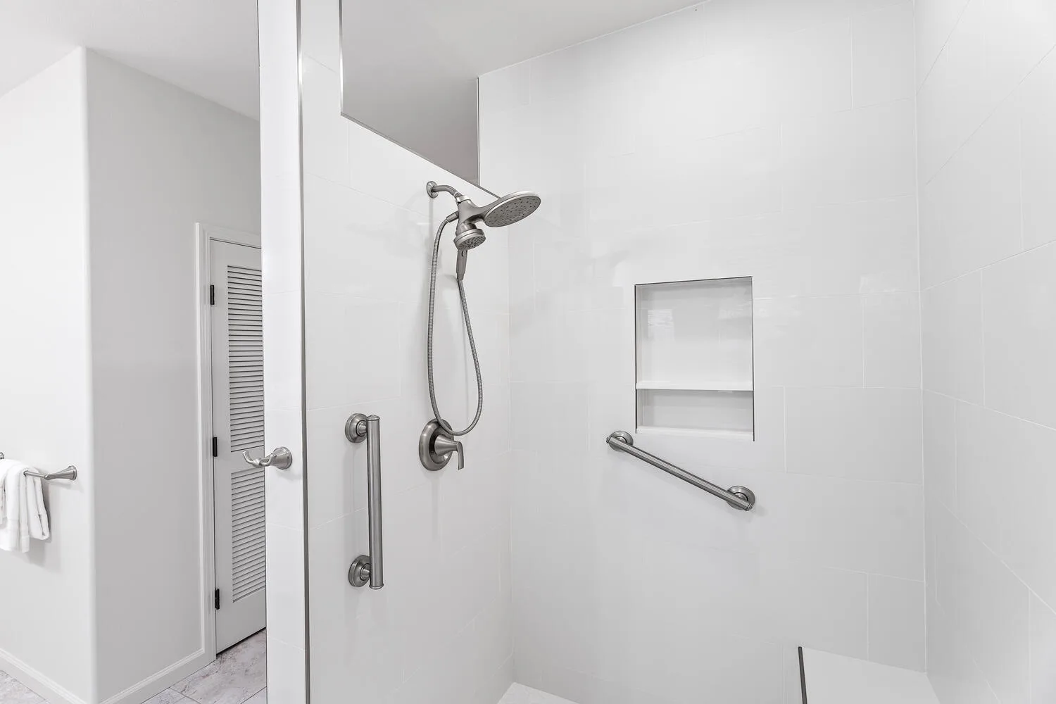 A bright tiled shower area with a handheld showerhead and wall grab bars.