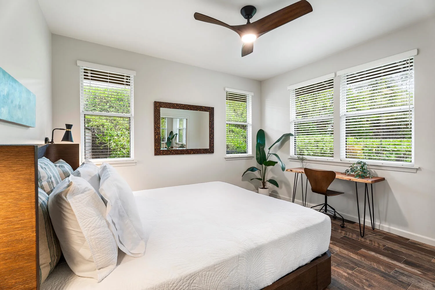 A bright bedroom with a large bed and windows fitted with blinds.