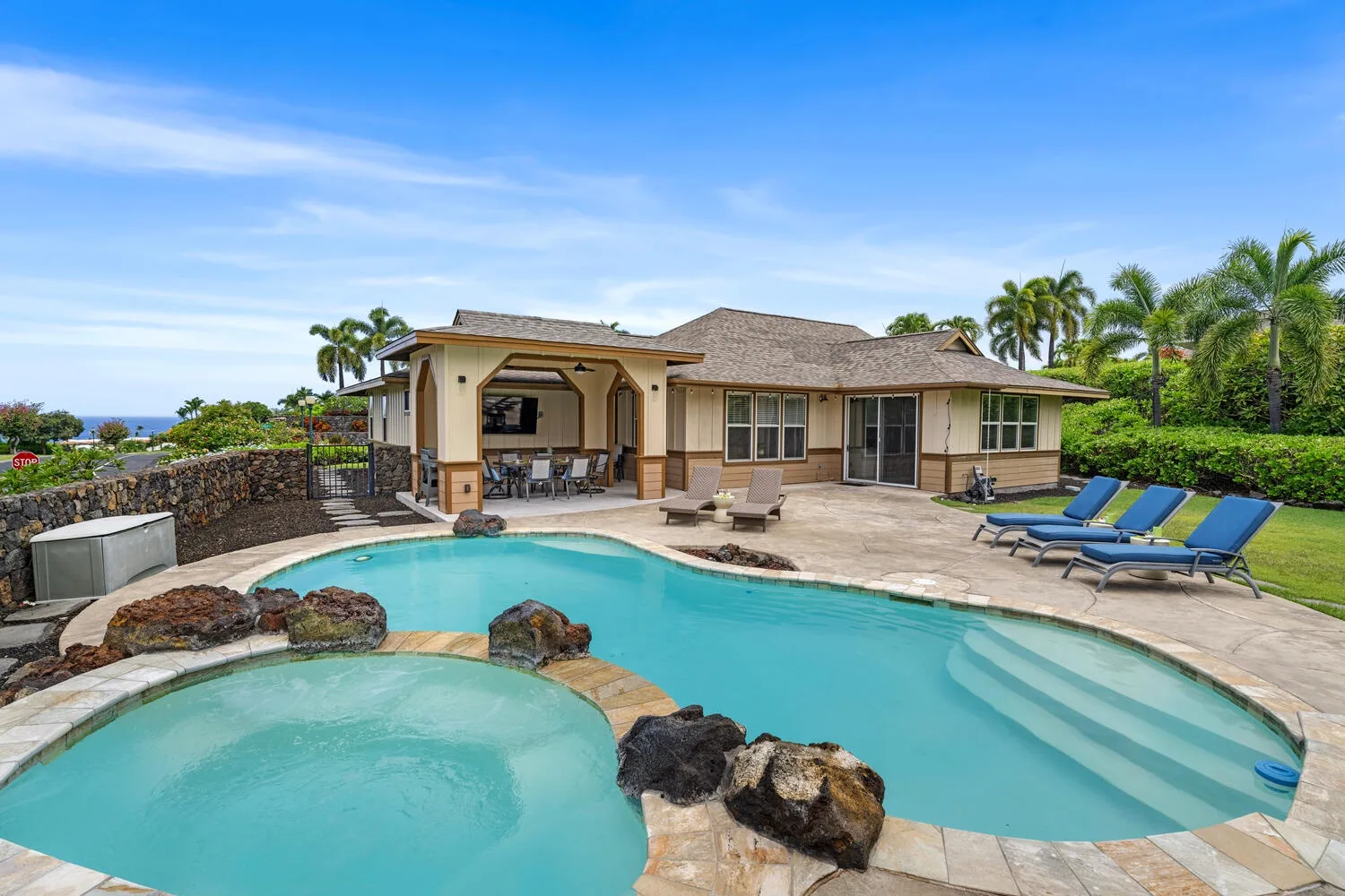 A curved outdoor swimming pool sits beside a single-story house and patio seating.