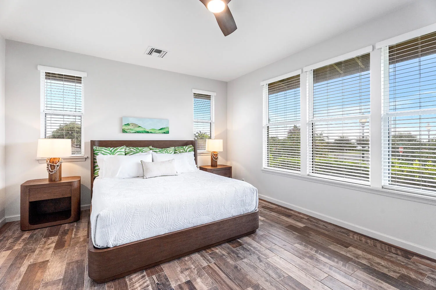 A bright bedroom with a bed, bedside tables, and large windows.