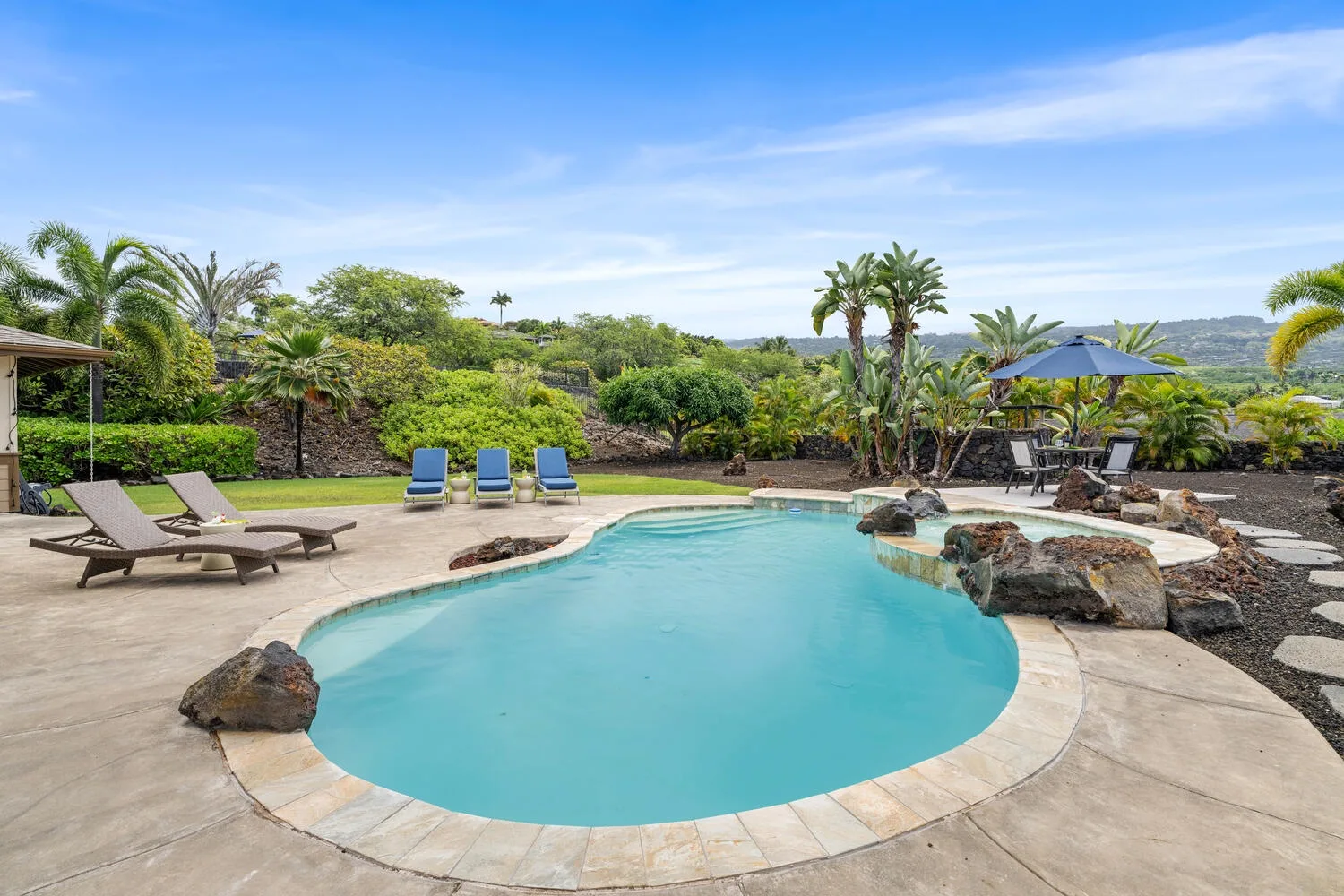 A curved swimming pool is surrounded by lounge seating and tropical greenery.