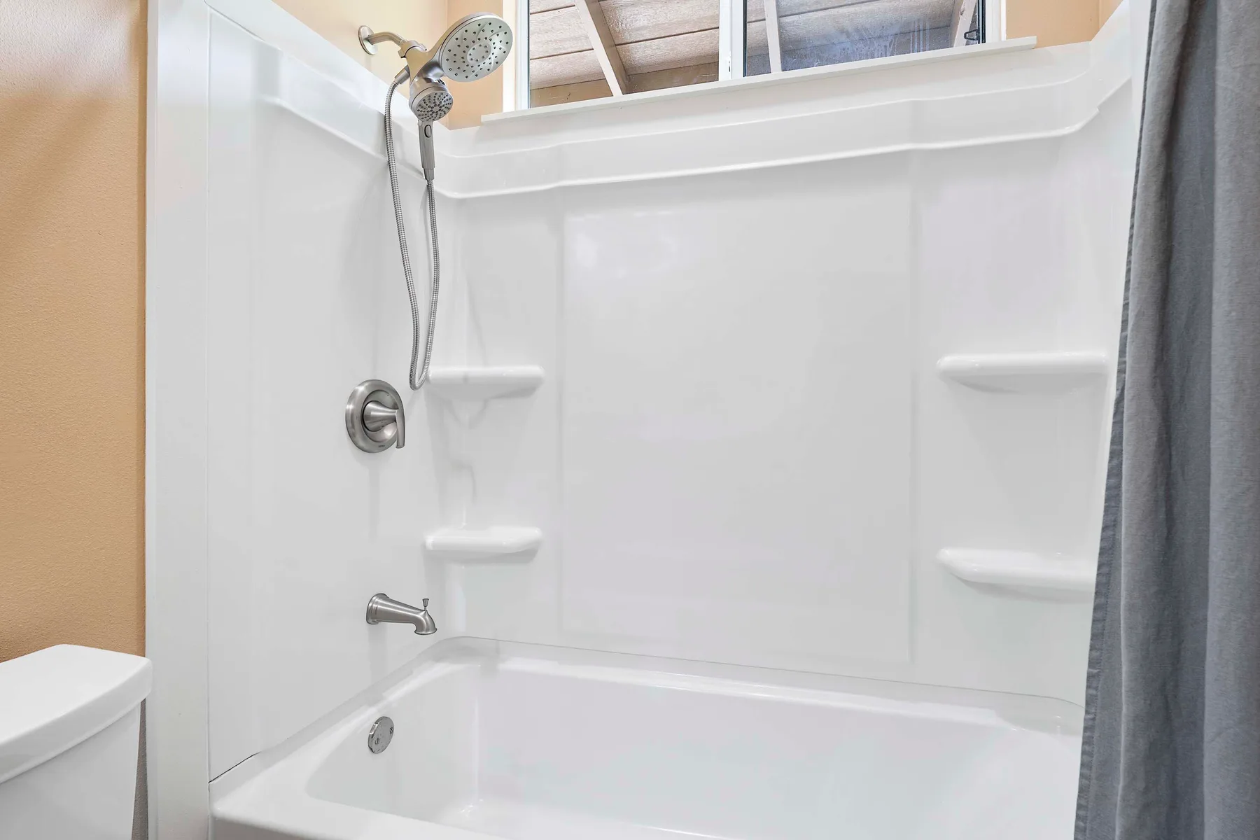 A white bathtub and shower with built-in shelves and a gray curtain.